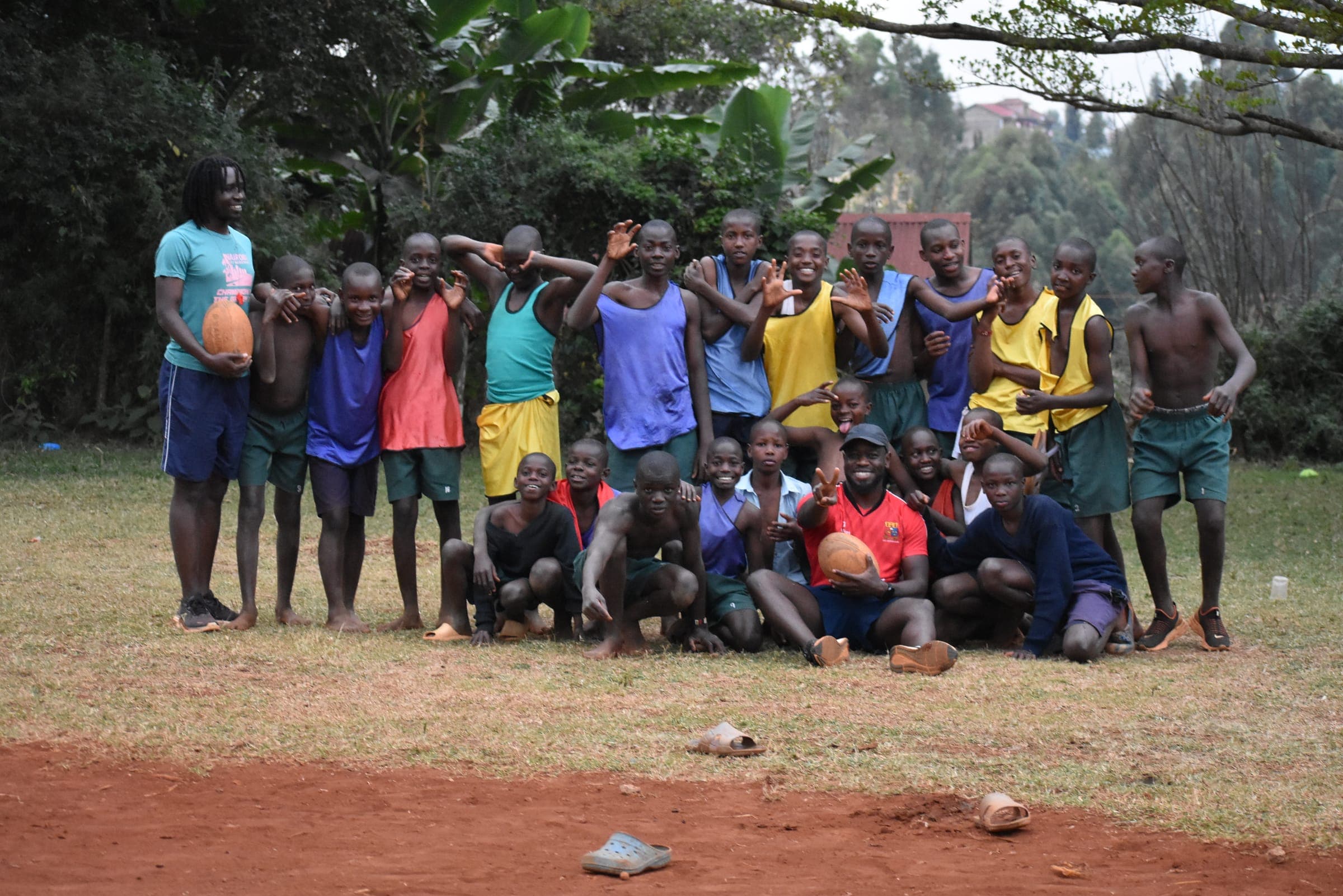 A large group of players and two coaches gathered on the grass at the end of a session, several raising their hands to the camera.
