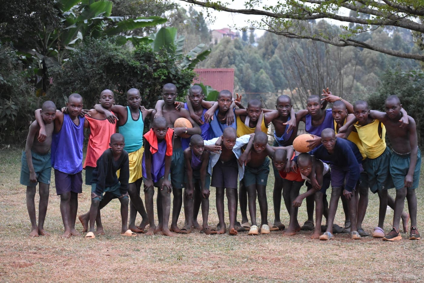 About twenty boys in training bibs standing arm in arm in a long line, two rugby balls held among them.